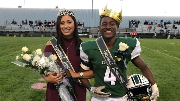 La reina del Homecoming con corona y banda y el jugador de fútbol americano con corona están en el campo de Westland High School.