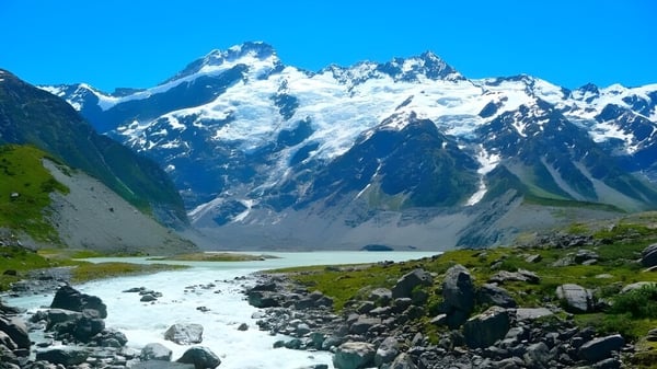 Un paisaje rocoso y cubierto de hierba con un arroyo fluyendo frente a montañas nevadas en el fondo cerca de Westland High School.