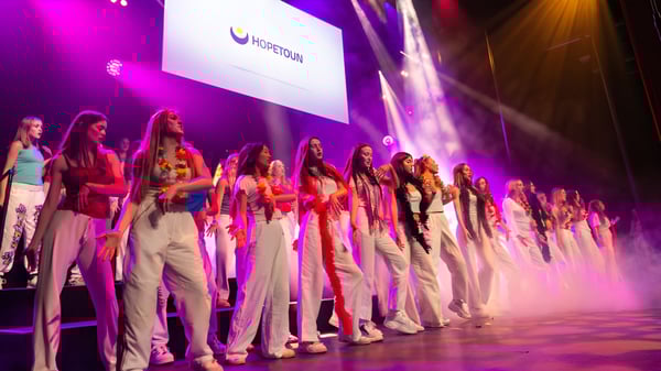 Un grupo de mujeres con ropa colorida está en el escenario de la Westminster School frente a un fondo iluminado.