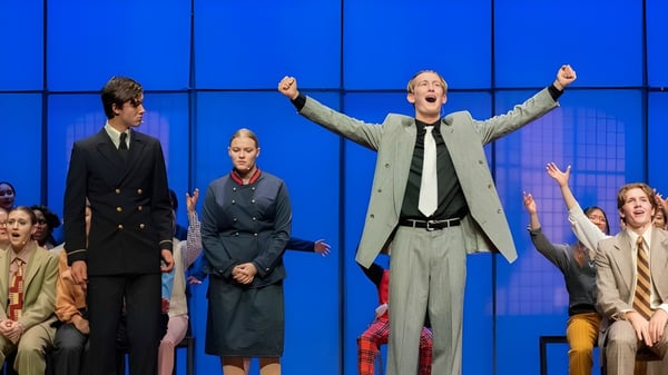 Estudiantes de la Westminster School presentan una obra de teatro en un escenario frente a un fondo azul.