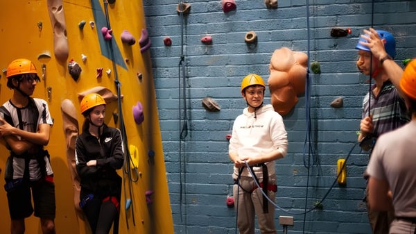 Alumnos de la Westminster School escalan con arneses y cascos en una colorida pared de escalada en el gimnasio de escalada.