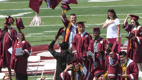 Las graduadas y graduados de la Westside Secondary School celebran su fiesta de graduación en un campo de césped con togas rojas.