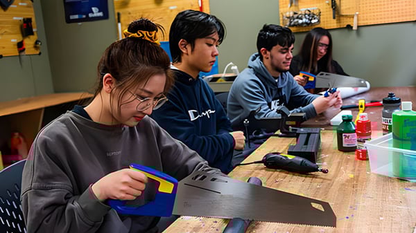 Un grupo de estudiantes de la Westsyde Secondary School trabaja juntos en una mesa con laptops y dispositivos electrónicos.