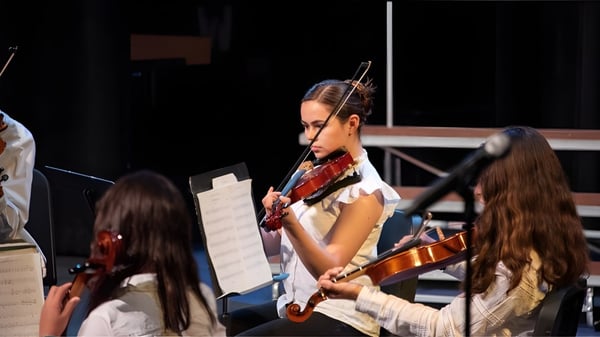 Una estudiante de la Westtown School toca el violín en el escenario rodeada de otros músicos.