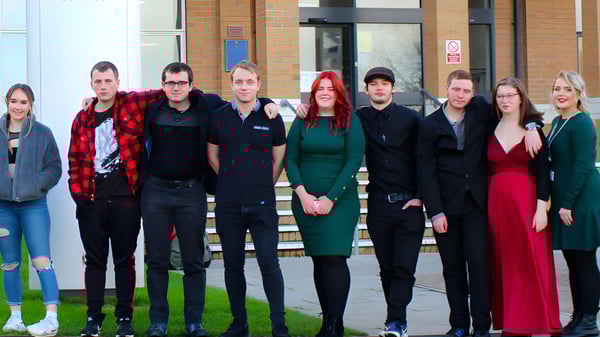 Un grupo de estudiantes está frente al edificio con fachada de vidrio en el campus del Weymouth College.