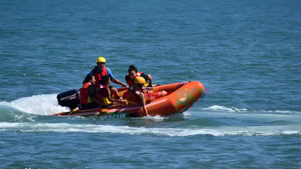 Dos estudiantes del Whanganui City College manejan un bote inflable naranja en el océano agitado.