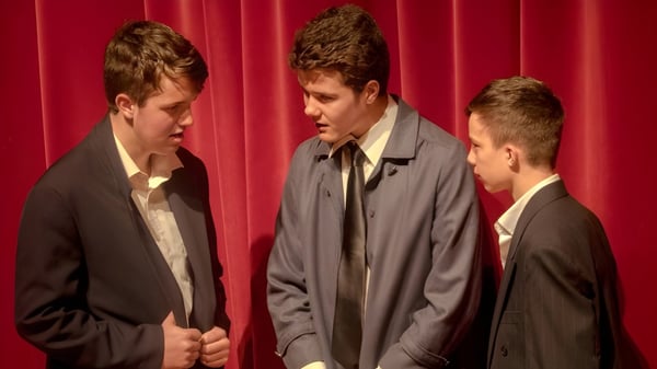 Tres estudiantes de la Whanganui Collegiate School están en ropa formal frente a una cortina roja.