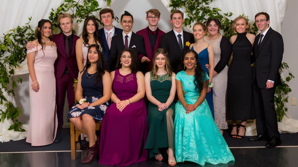 Un grupo de personas vestidas formalmente posan frente a un fondo de flores en el terreno de la Whanganui High School.
