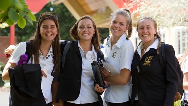 Cuatro alumnas en uniforme escolar están juntas y sonríen en el campus de la Whangarei Girls High School.