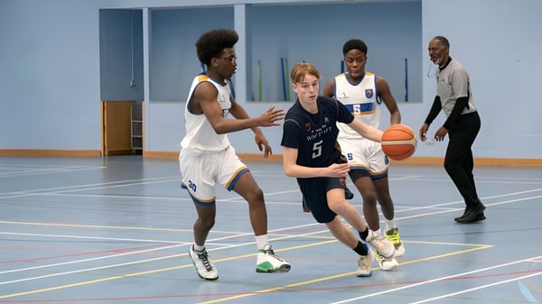 Un grupo de estudiantes de la Whitgift School juega al baloncesto en la cancha de baloncesto con suelo azul.