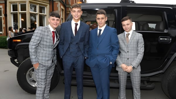 Un grupo de estudiantes de la Whitgift School en trajes está frente a un gran vehículo negro en una calle de la ciudad.