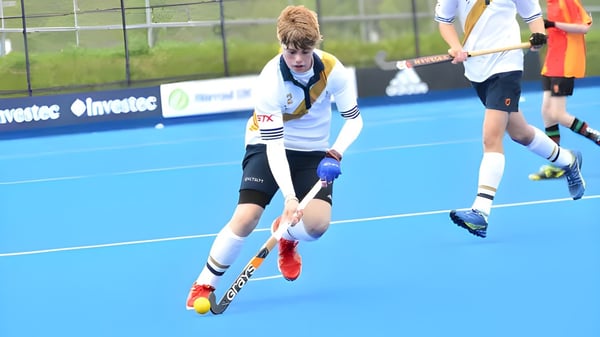 Un estudiante de la Whitgift School juega al hockey sobre césped en el campo de césped artificial azul con otros jugadores al fondo.