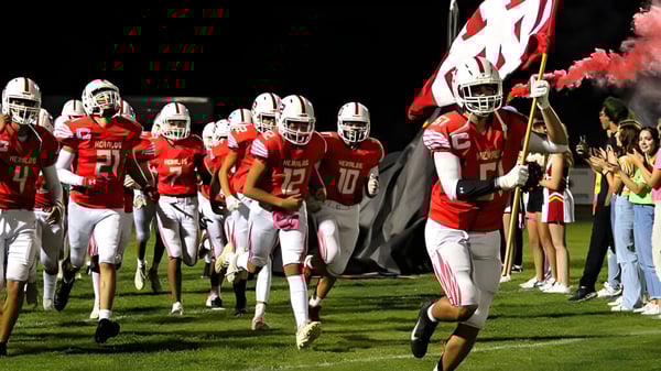 Los jugadores de fútbol de la Whittier Christian High School corren juntos hacia el campo mientras se pueden ver animadoras y espectadores en el fondo.