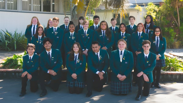Un grupo de estudiantes está al aire libre en el campus del William Colenso College frente a árboles y edificios.