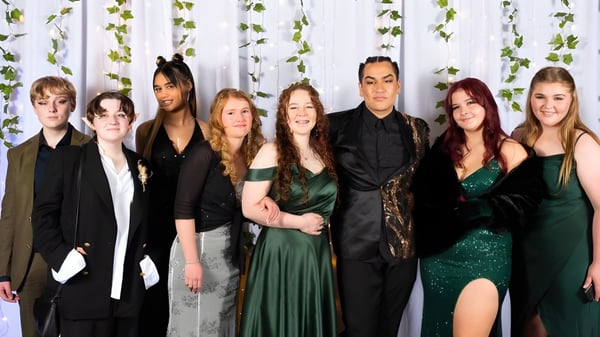 Un grupo de estudiantes en ropa formal está frente a un fondo verde en el campus del William Colenso College.