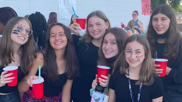 Un grupo de jóvenes mujeres de la Williams Field High School está junto y sostiene vasos rojos.