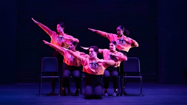 Un grupo de estudiantes de la Williston Northampton School realiza una actuación de baile en un escenario oscuro con trajes coloridos.