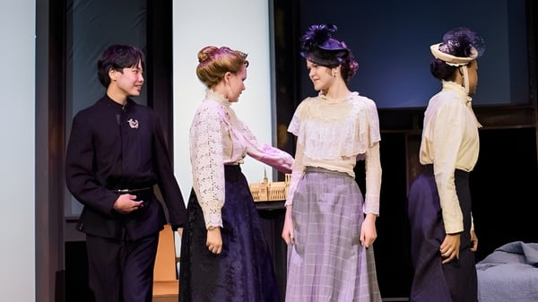Cuatro estudiantes de la Williston Northampton School están en trajes y peinados elaborados en un escenario con fondo oscuro.