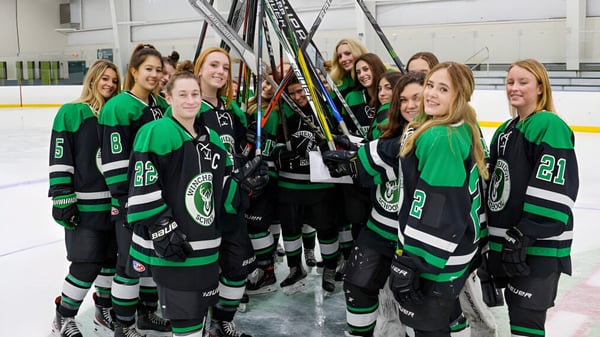 Un grupo de jóvenes jugadoras de hockey en camisetas verdes y negras sobre el hielo de la Winchendon School en Massachusetts.