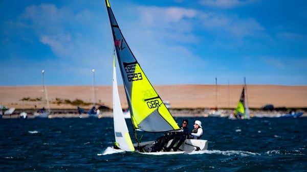 Un velero con vela amarilla navega sobre el agua frente a la costa del Winchester College.