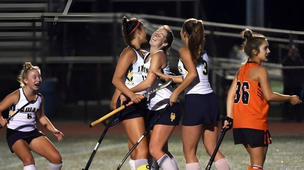 Un grupo de deportistas femeninas se reúne en ropa deportiva en el campo de deportes de la Windermere School de noche bajo la luz artificial.