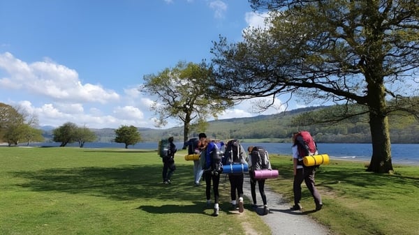 Estudiantes de la Windermere School caminan en un campo cerca de un cuerpo de agua con árboles y cielo azul.