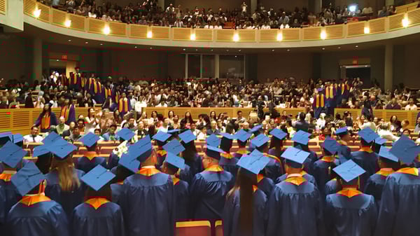 Los graduados de la Windermere Secondary School están sentados en un aula decorada festivamente con togas de graduación azules y naranjas.
