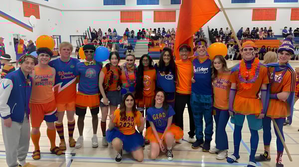 Un gran grupo de estudiantes de la Winston Churchill High School está en sus uniformes naranja-azul en un gimnasio.