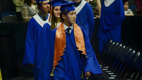 Un grupo de graduados en togas azules y naranjas está en una ceremonia de graduación de la Winston Churchill High School.
