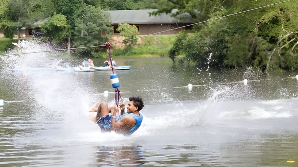 Un estudiante de la Winston Salem Christian School está haciendo wakeboard detrás de un barco en el agua.
