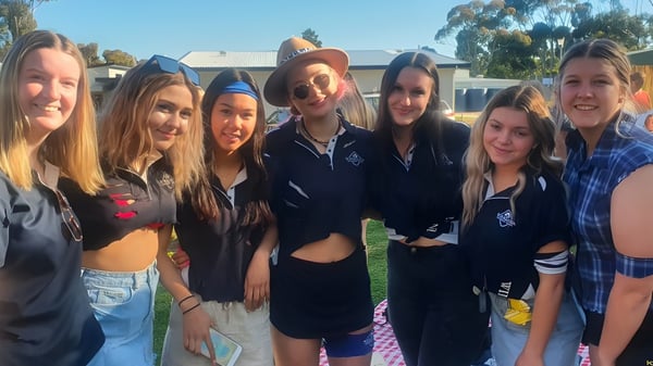 Un grupo de estudiantes está afuera en el terreno de la Wirreanda Secondary School frente a un edificio y árboles.
