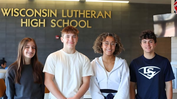 Cuatro estudiantes están de pie frente al cartel de la Wisconsin Lutheran High School.