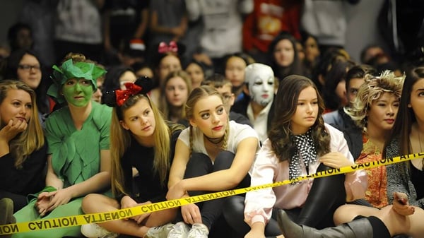 Un grupo de personas disfrazadas está sentado detrás de un cordón policial en un evento en la W.J. Mouat Secondary School.