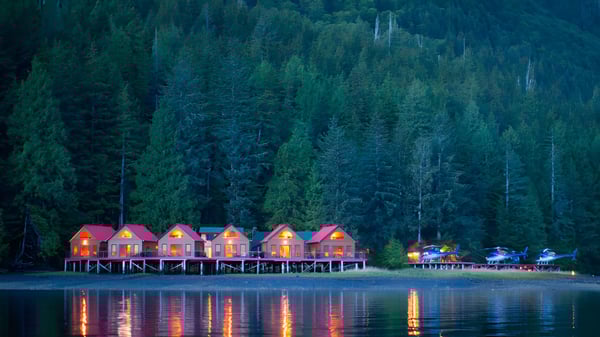 Lago tranquilo con cabañas de colores y un bosque al fondo cerca de la W.J. Mouat Secondary School.