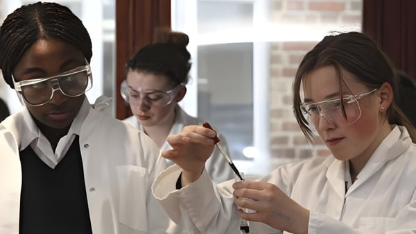 Tres estudiantes de la Woldingham School trabajan concentrados en el laboratorio con batas blancas y gafas de protección.
