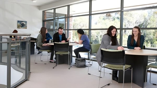 Un grupo de estudiantes de la Wollongong University discute juntos en una oficina moderna de vidrio.