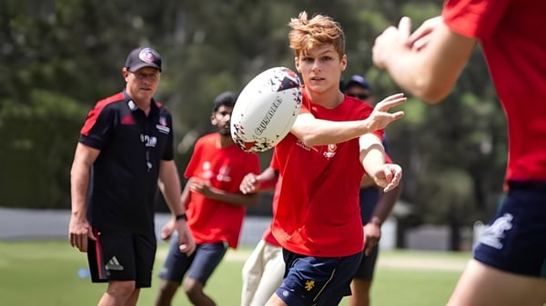 Un joven en camiseta roja corre con un balón de rugby por el campo en el campus de la Wollongong University.