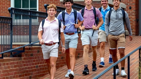 Un grupo de estudiantes de la Woodberry Forest School camina juntos por un camino pavimentado frente a un edificio con grandes ventanas.
