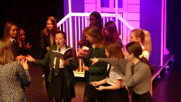 Un grupo de estudiantes de la Woodbridge School está en un escenario con iluminación colorida en el salón de teatro.