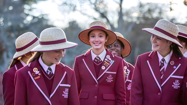 Un grupo de jóvenes alumnas en ropa uniforme está en el terreno de Woodford House frente a unos árboles.
