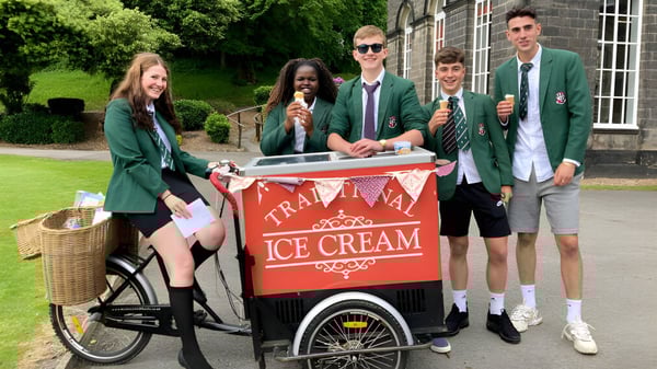 Estudiantes de la Woodhouse Grove School están alrededor de un carro de helados en un campo frente a un edificio de ladrillo.