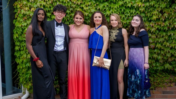 Seis personas en ropa formal posan frente a una pared cubierta de hiedra en el terreno de la Woodhouse Grove School.