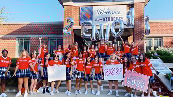 Estudiantes de la Woodlands Academy of the Sacred Heart dan la bienvenida a los nuevos estudiantes de la promoción 2022 frente a un edificio de ladrillo.