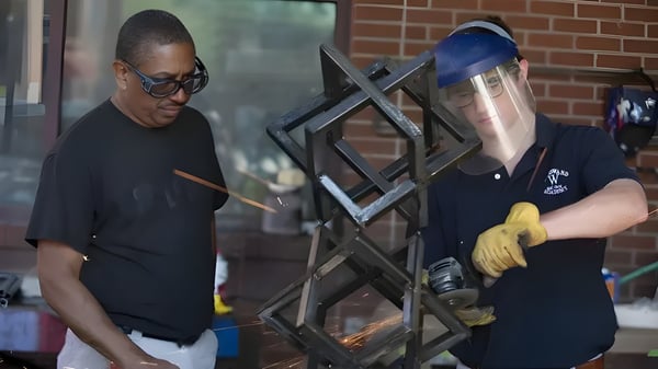 Dos personas trabajan en un marco de metal frente a una pared de ladrillo en el terreno de la Woodward Academy.