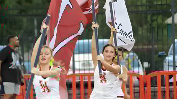 Estudiantes de la Woodward Academy sostienen banderas y pancartas en una demostración pública frente a un área cercada.