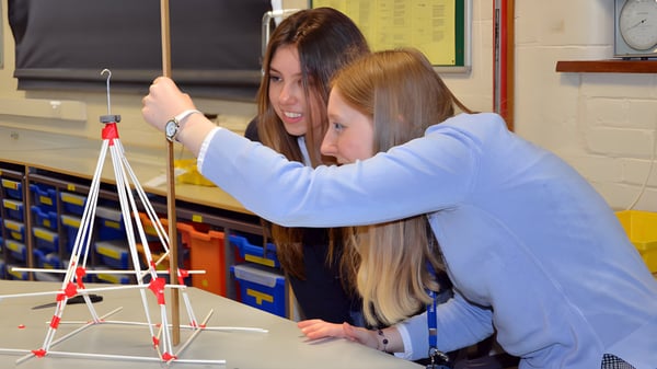 Dos estudiantes de Worth School construyen en un aula una estructura con varillas y conectores de colores.