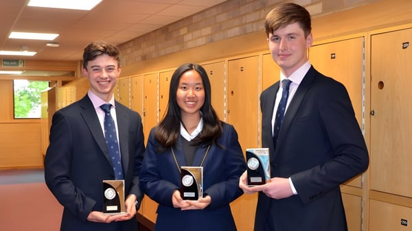 Tres estudiantes de Worth School están en el pasillo frente a los casilleros y sostienen premios en las manos.