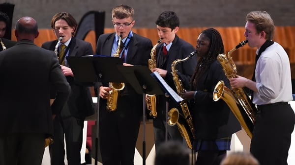 Estudiantes de Worth School están vestidos de manera formal en un escenario y se preparan con instrumentos musicales para una actuación.