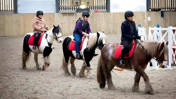 Tres personas vestidas para montar participan en la clase de hípica de la Worthgate School Canterbury en una pista de equitación.
