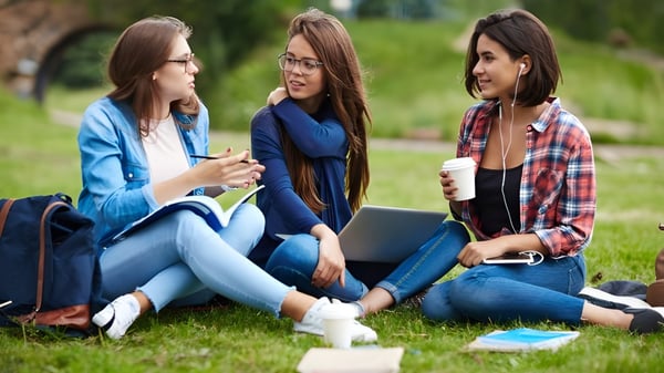 Tres estudiantes de la Worthgate School Canterbury están sentadas en la pradera y conversan frente a un fondo verde.